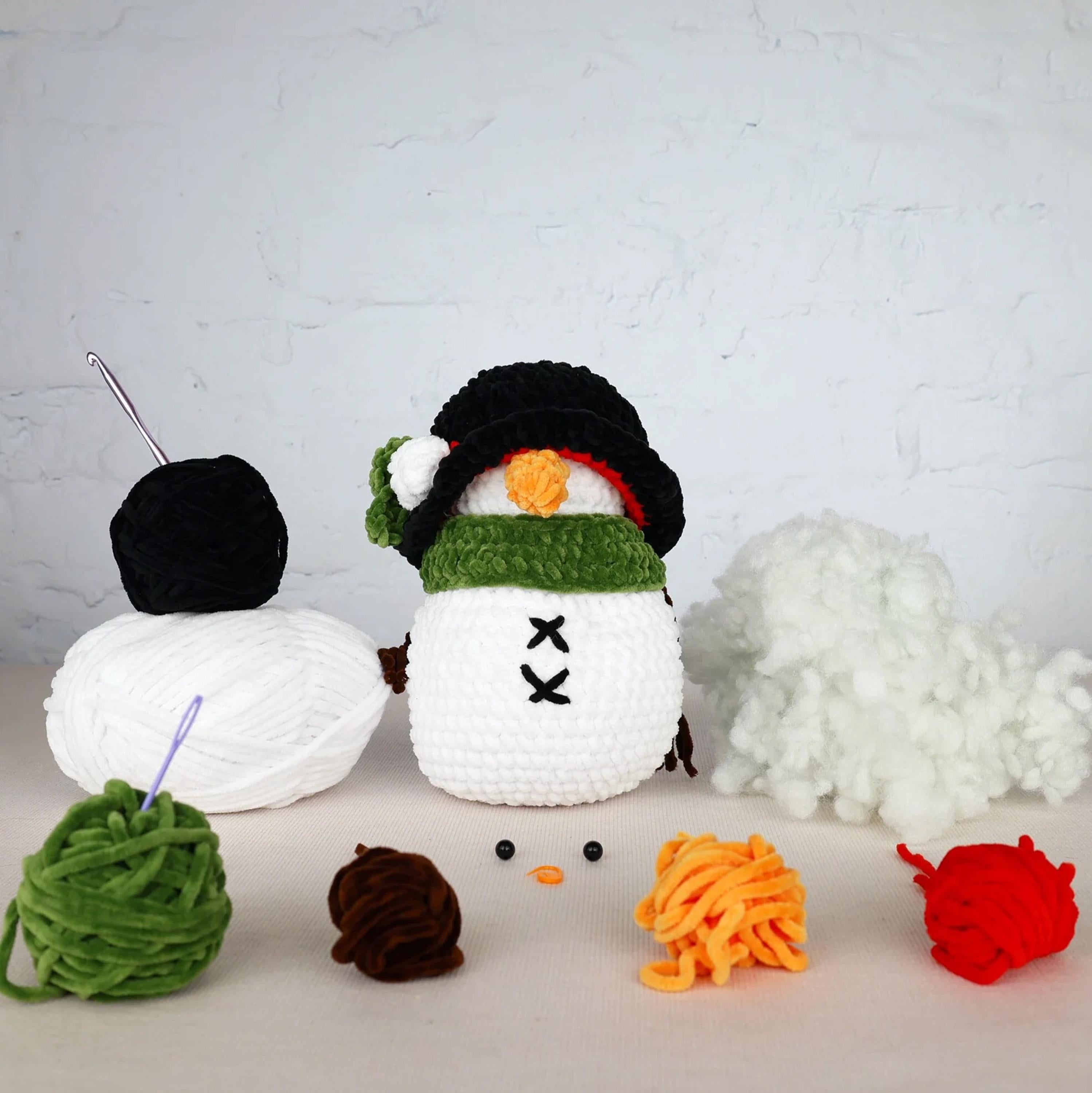 A crocheted snowman toy surrounded by various crochet yarn balls and a crochet hook, along with some additional crochet materials.